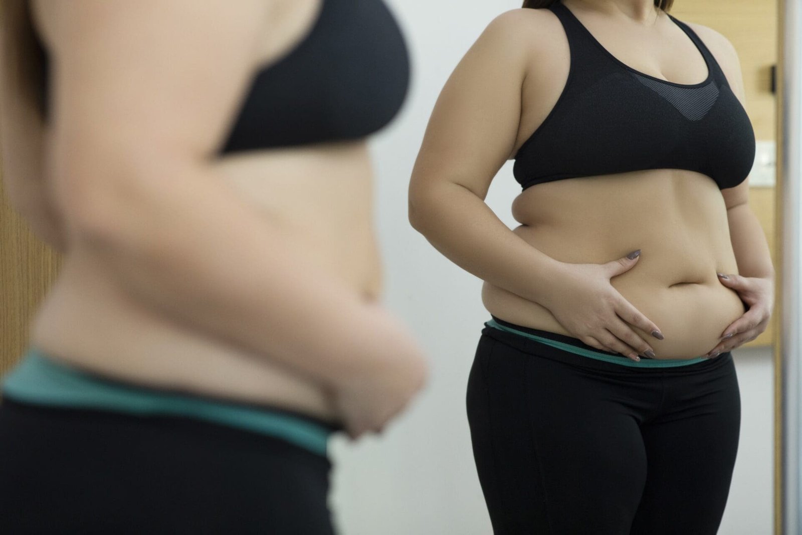 Woman looking at her midsection in the mirror, representing body image concerns and the journey of medical weight loss with Ozempic alternatives.